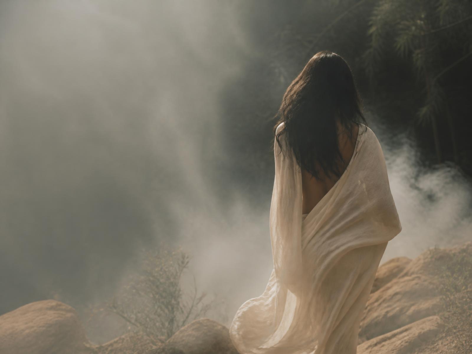 Mujer envuelta en tela de lino caminando entre niebla y luz natural